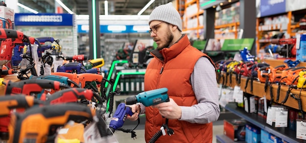 El constructor en una tienda de herramientas eléctricas elige un nuevo taladro y destornillador