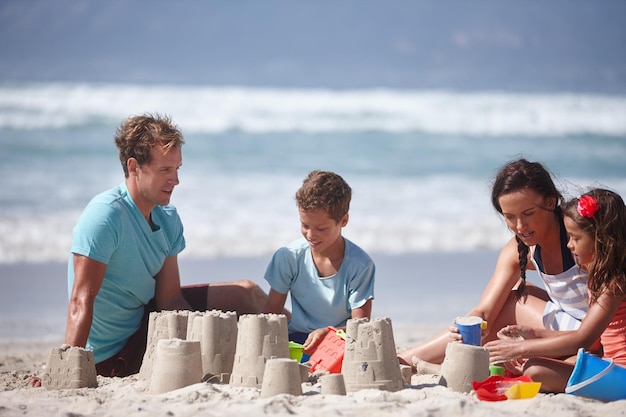 Construir castillos de arena, uno de los placeres simples de la vida Foto de una familia feliz construyendo castillos de arena juntos en la playa