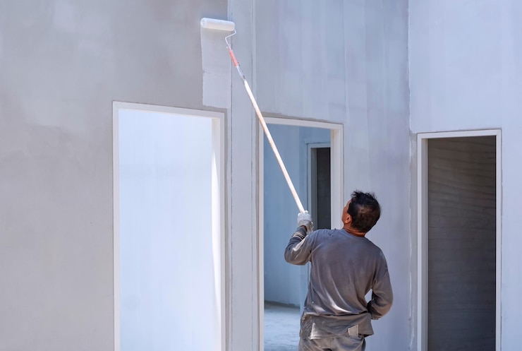 Foto construtor asiático pintando cor branca na parede de concreto dentro do canteiro de obras