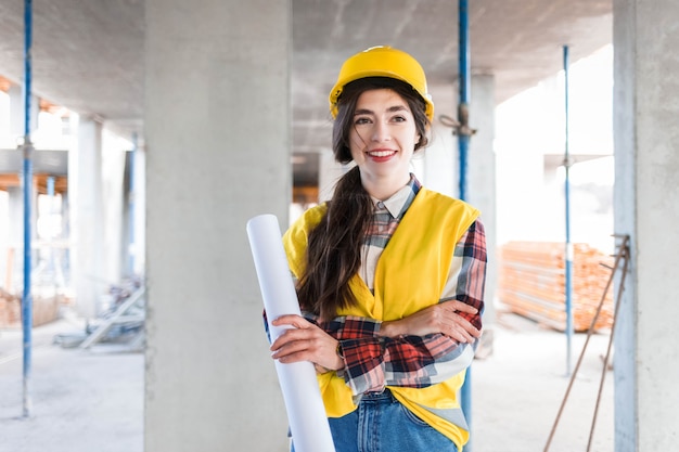 Foto construtor de engenheiro confiante garota fica em um canteiro de obras, segurando o papel com desenhos