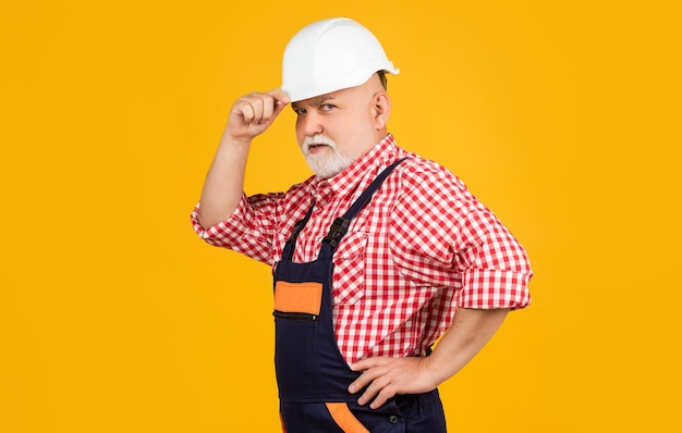 Construtor de homem envelhecido sério no capacete em fundo amarelo