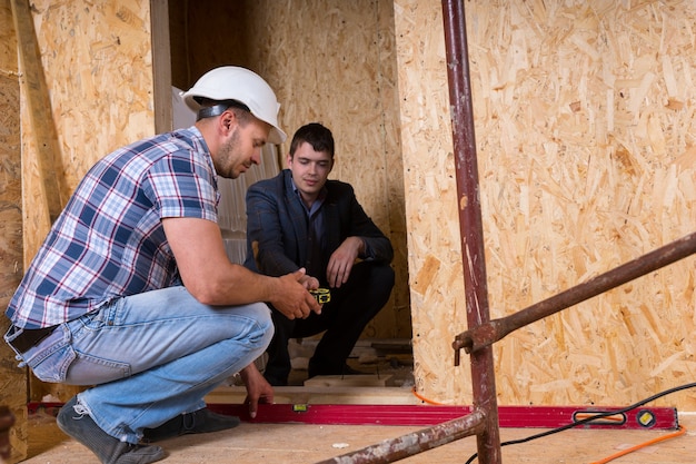 Construtor e arquiteto trabalhando juntos e inspecionando o nível uniforme da nova porta da casa dentro do canteiro de obras, para precisão e controle de qualidade