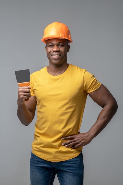 Construtor. Jovem feliz e atraente afro-americana com um capacete de construção brilhante e uma lâmina de trabalho na mão