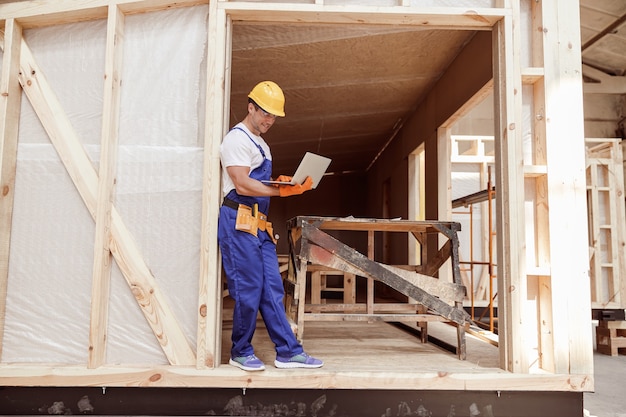 Construtor masculino alegre usando laptop no canteiro de obras