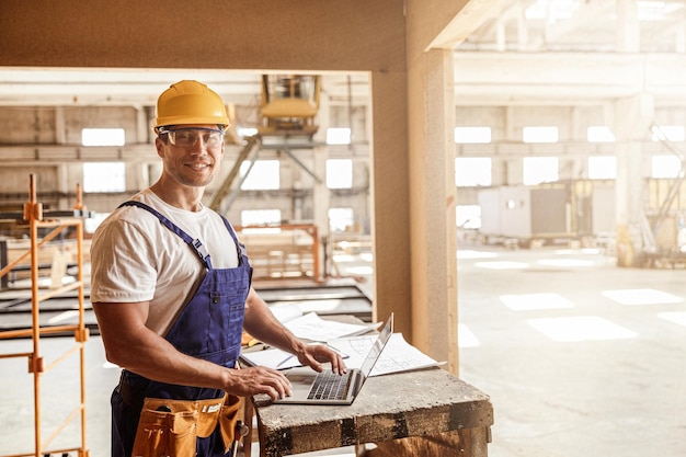 Construtor masculino alegre usando laptop no canteiro de obras