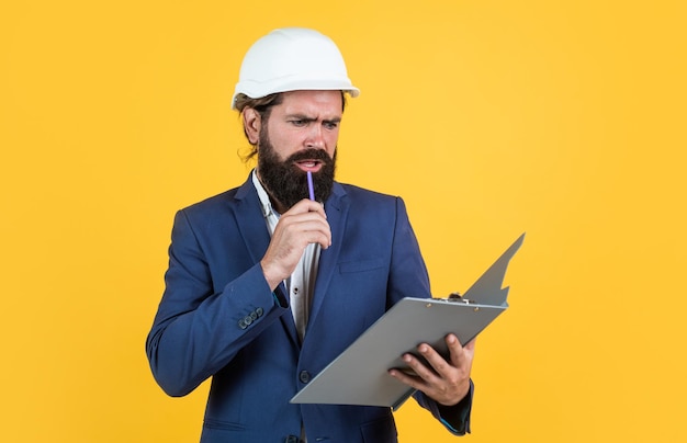 Construtor masculino assistente vestindo terno formal e capacete para proteção trabalhando no projeto de construção homem concentrado com barba usa conceito de capacete de arquitetura de engenharia e construção