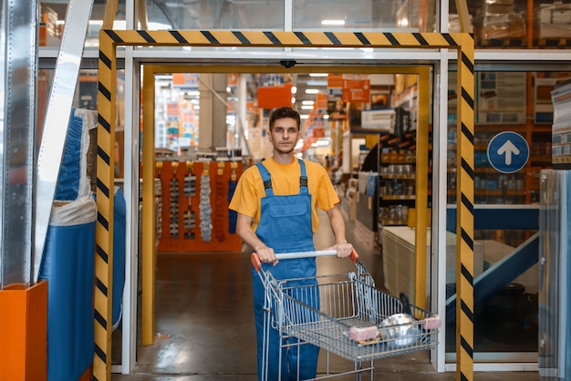 Construtor masculino carrega materiais de construção em um carrinho, loja de ferragens. o cliente olha as mercadorias na loja de bricolagem