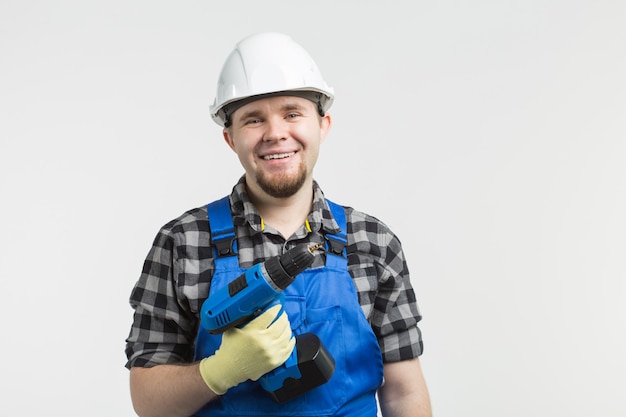 Construtor masculino caucasiano feliz com chave de fenda na parede branca, usando capacete branco.