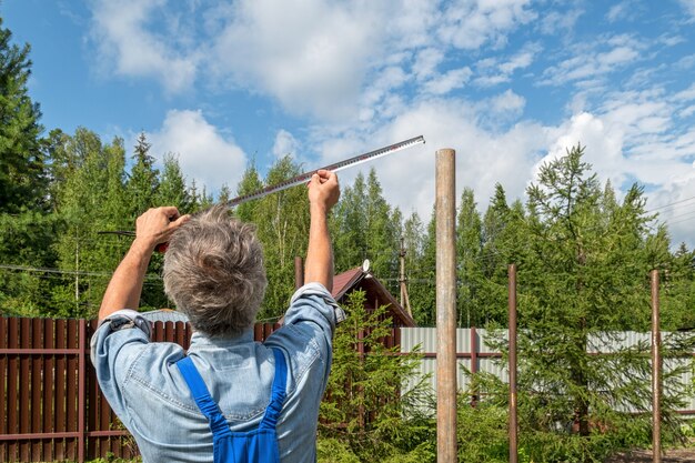 Construtor masculino com uma fita métrica em um canteiro de obras real na natureza. Mede a distância entre os postes com uma fita métrica.