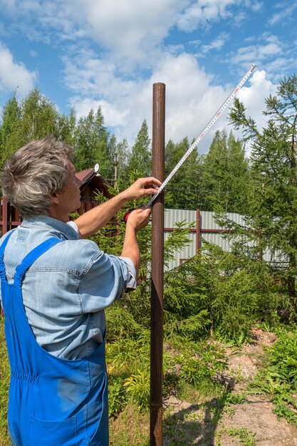 Construtor masculino com uma fita métrica em um canteiro de obras real na natureza. Mede a distância entre os postes com uma fita métrica.