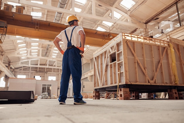 Construtor masculino em macacão de trabalho observando prédio em construção