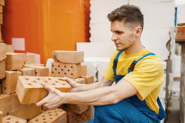 Construtor masculino escolhendo tijolos na loja de ferragens. Construtor de uniforme olha as mercadorias na loja de bricolage