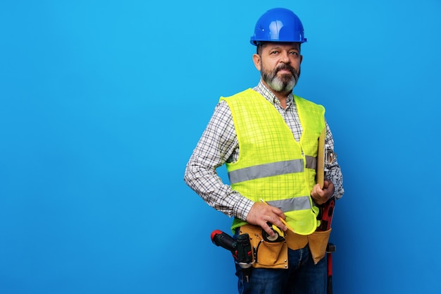 Construtor masculino ou faz-tudo de uniforme segurando uma prancheta contra um fundo azul