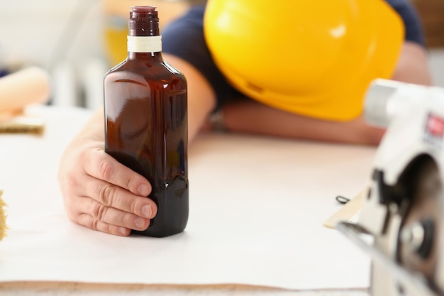 Construtor sedento e cansado no capacete de segurança se sente exausto e segura garrafa de álcool de conhaque