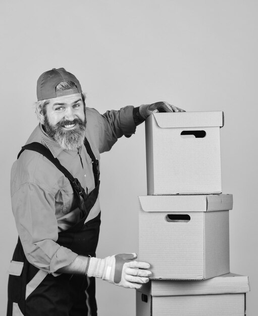 Construya su futuro usted mismo cargador barbudo en uniforme Cajas de cartón que se mudan a una nueva casa compra de una nueva habitación o reparación de la habitación Hombre que usa cajas de embalaje de traje de baño se muda a un nuevo apartamento