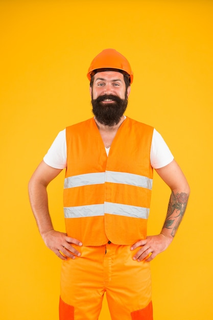 Construyendo mañana. Hombre barbudo sonriendo en ropa de trabajo protectora para la actividad de construcción. Contructor de renovación de edificio feliz sobre fondo amarillo. Industria de la edificación y la construcción.