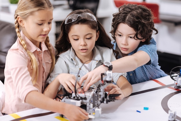 Construyendo robot juntos. Científicos inteligentes, amigables y hábiles sentados en la escuela y disfrutando de la clase mientras expresan interés y construyen un robot