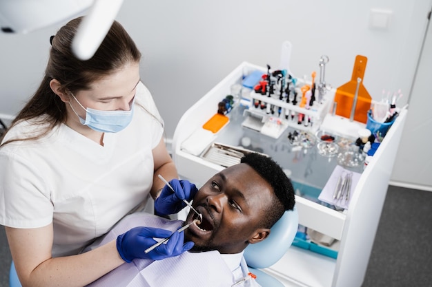 Consulta com dentista em odontologia Tratamento de dentes Dentista examina a boca e os dentes do homem africano e trata dores de dente Homem africano paciente de odontologia