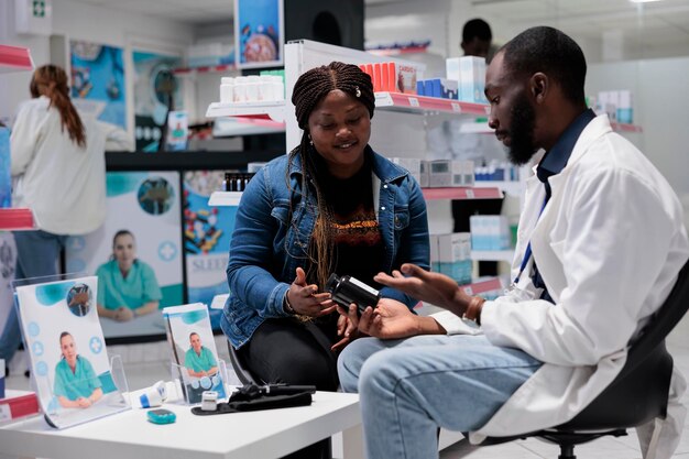 Consulta de farmácia, cliente afro-americano comprando frasco de comprimidos na farmácia, farmacêutico aconselhando vitaminas. Cliente tomando prescrição de medicamentos, químico e paciente, toda equipe negra