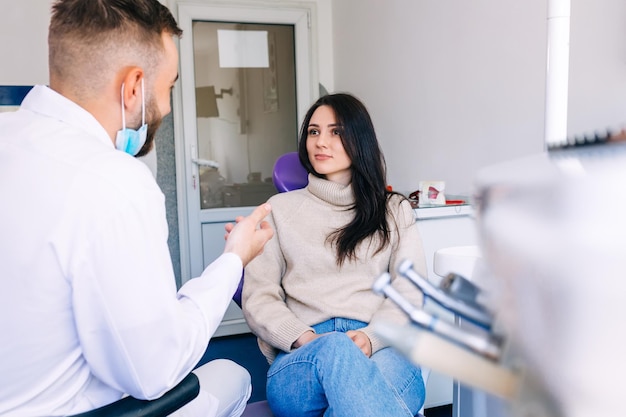 Consulta de dentista sobre su estado de paciente. niña sentada en una silla y escuchando a un ortodoncista. clínica.