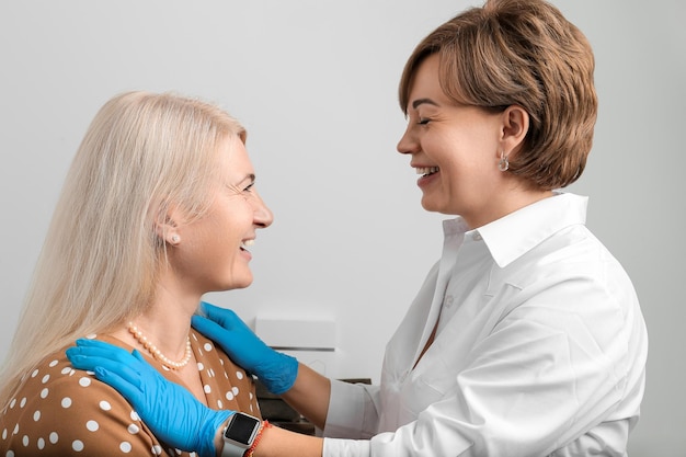 Consulta em uma clínica de cosmetologia Médico profissional cosmetologista e mulher adulta estão sorrindo e discutindo procedimentos para rejuvenescimento facelift