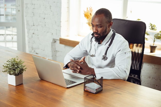 Consulta médica para paciente, tranquilo y alegre. Médico afroamericano durante su trabajo con pacientes, explicando recetas de medicamentos. Trabajo arduo diario para la salud y salvar vidas durante la epidemia.