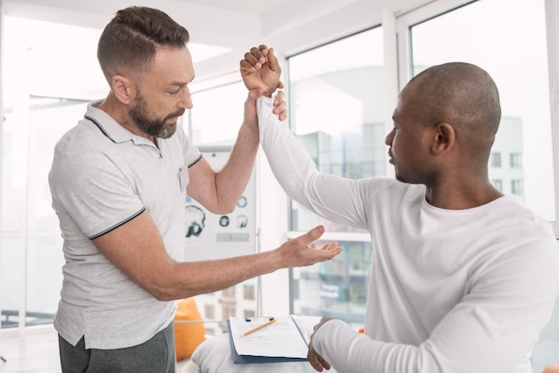 Consulta médica. Terapeuta profissional sério segurando o braço do paciente enquanto olha para ele