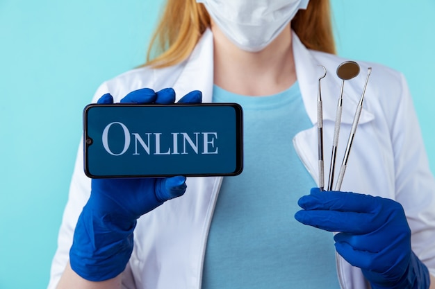 Consulta online ao dentista a partir do seu telefone. médica segurando instrumentos médicos e móveis isolados sobre o fundo azul.