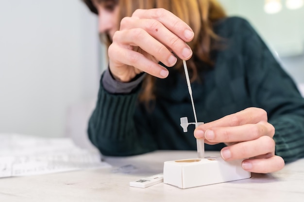 Consultar instrucciones con el hisopo en el líquido reactivo. Una mujer joven que realiza la prueba rápida de antígenos en su casa, sars-cov-2, coronavirus, covid-19