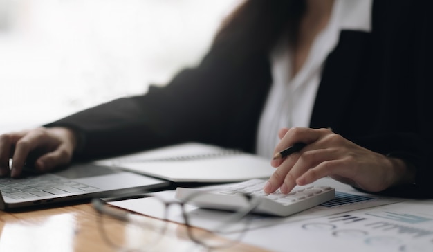 Consulte o conceito financeiro. Mulher de negócios apontando para a calculadora e usando o computador portátil.