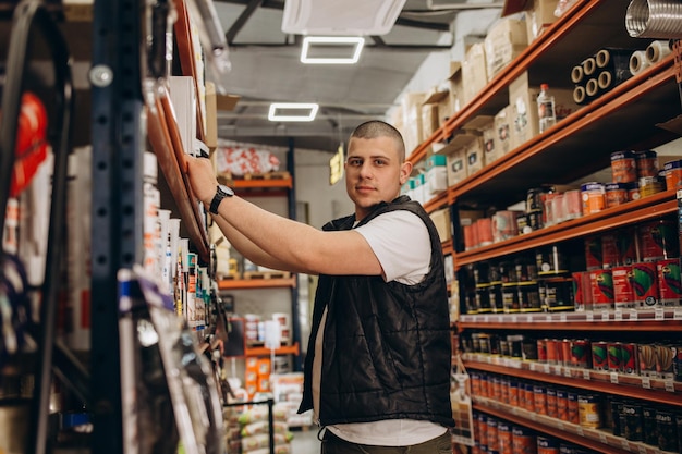 Consultor caucasiano de uniforme na loja de ferragens Homem parado ao lado de prateleiras com ferramentas na loja