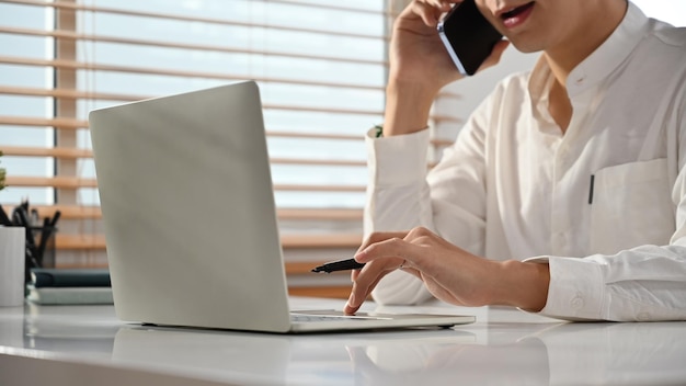 Consultor financeiro masculino sorridente consultando cliente distante por telefonema e usando laptop no local de trabalho