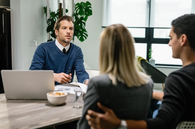 Consultor financiero comunicándose con una pareja mientras revisa las finanzas de su hogar