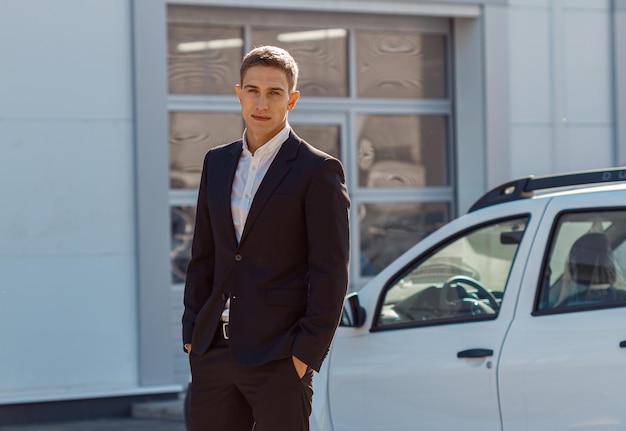 Consultor masculino joven en auto show de pie cerca de los coches y mirando a la cámara