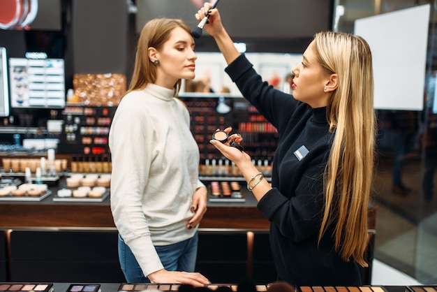 Consultor vendedor y mujer probando polvos en la tienda de maquillaje.