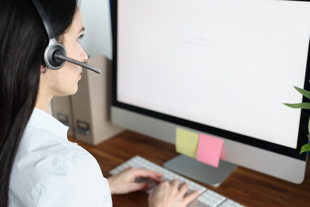 Consultora em fones de ouvido com microfone sentada na frente do monitor do computador