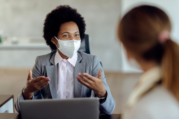 Consultora financeira negra conversando com seu cliente e usando máscara protetora durante a reunião