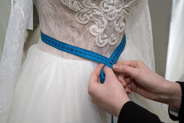 Una consultora en una tienda mide un vestido de novia con cinta métrica