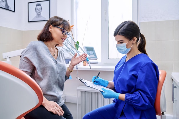 Foto consultório odontológico visita paciente do sexo feminino conversando com médico dentista fazendo anotações