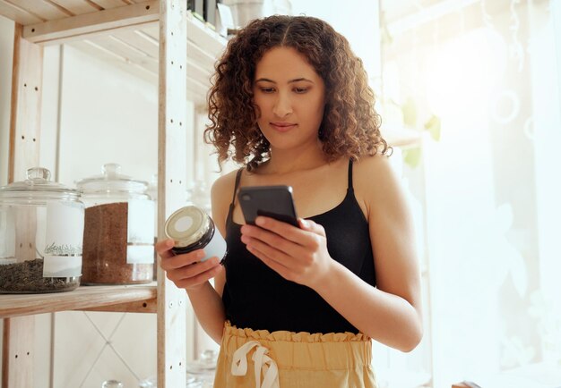 Consumidor femenino o cliente con teléfono buscando información de productos orgánicos en línea para veganos éticos o ingredientes saludables Comprador ecoconsciente leyendo la etiqueta tarro de grano de café hecho localmente en la tienda