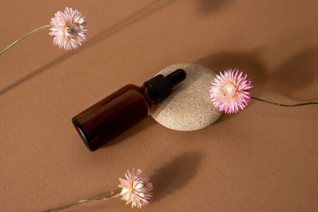 Conta-gotas de vidro marrom com óleo cosmético com flores rosa secas na vista frontal do plano de fundo de terracota, close-up