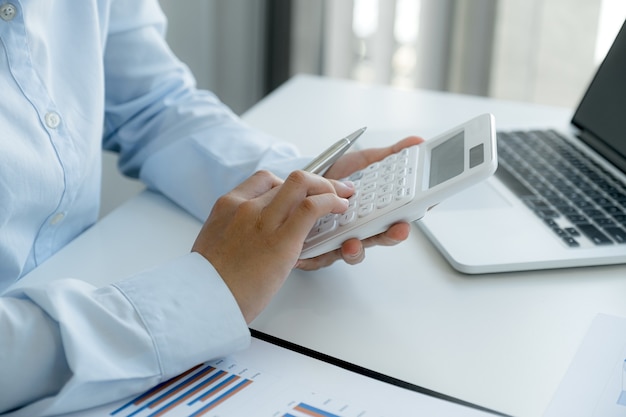 Foto contable de mujeres empresarias utilizan calculadora y portátil haciendo cuenta para pagar impuestos en el escritorio blanco en la oficina de trabajo.