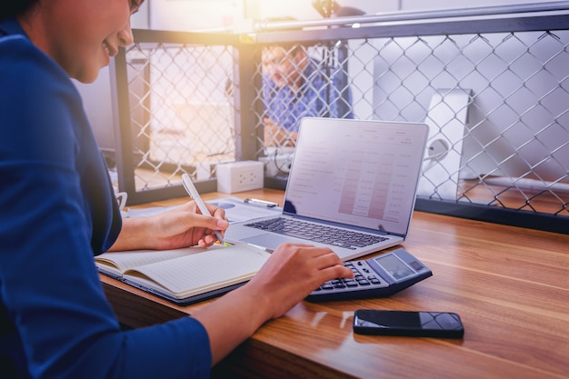 Contador de mulher que trabalha usando a calculadora para calcular o relatório financeiro no local de trabalho.