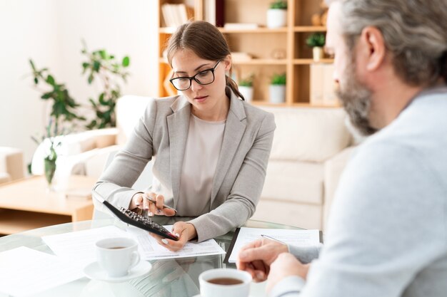 Contador joven con calculadora presionando sus botones mientras consulta con un colega por lugar de trabajo en la reunión