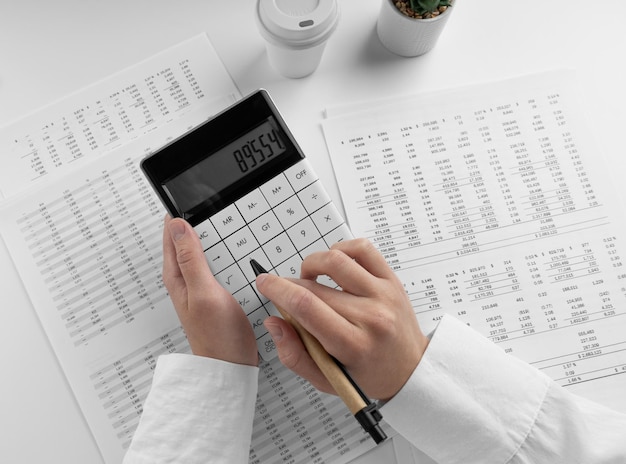 Contador usando calculadora no escritório de mesa em fundo branco com visão superior do demonstrativo financeiro