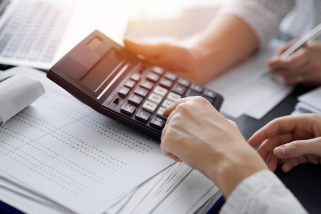 Contadora usando uma calculadora e um computador portátil enquanto conta os impostos para um cliente.