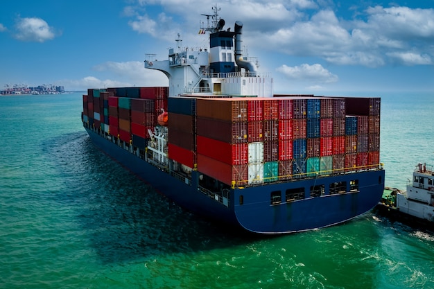 Containerschiff segeln im grünen Meer und Schlepper ziehen und blauen Himmel