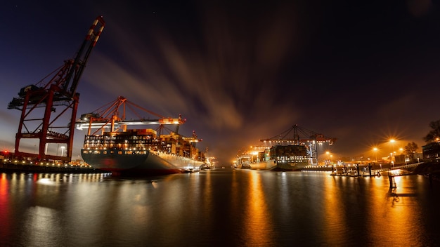 Containerterminal mit Containerschiffen, Kränen und Containern in der Nacht mit wunderschönen Wolken