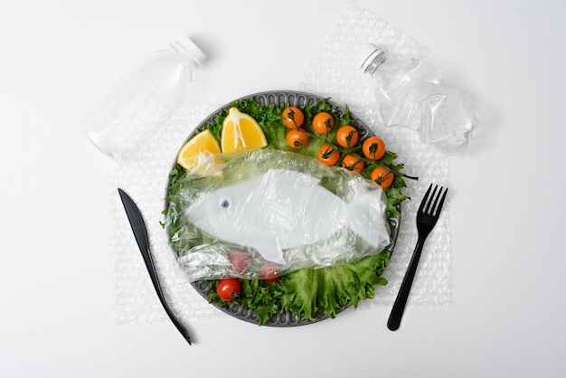 Contaminación del concepto de peces oceánicos del mundo peces de plástico con verduras en un plato de basura plástica sobre fondo blanco