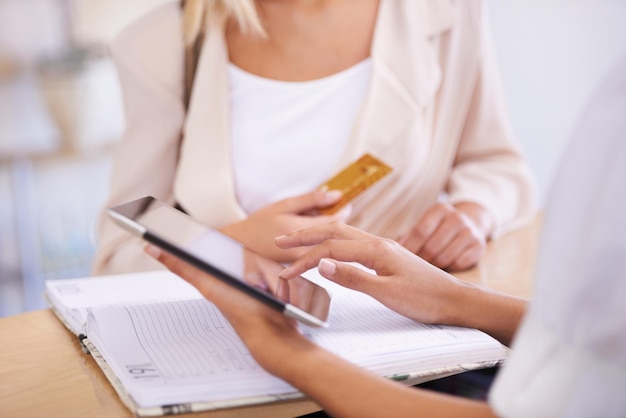 Contando sus cargos Una mujer joven entregando su tarjeta de crédito a un empleado de ventas